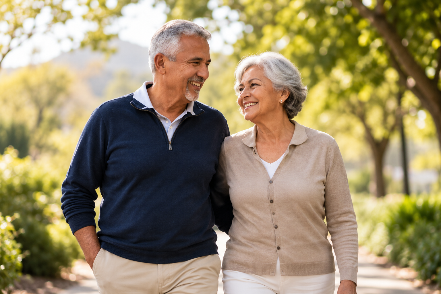 An older couple smiling at each other while walking in a park.